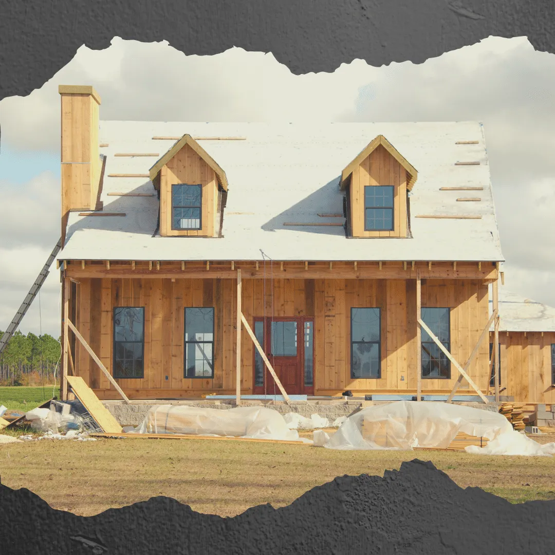 A two-story house under construction with exposed wooden framing, incomplete roofing, and surrounding construction debris.