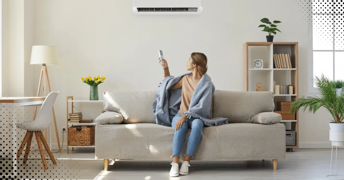 Woman sitting on a living room sofa raising her arms happily, with plants and décor around her, symbolizing clean indoor air and a healthy home environment