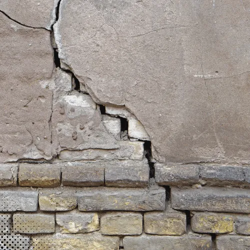 Cracked exterior wall showing damaged plaster and exposed brick