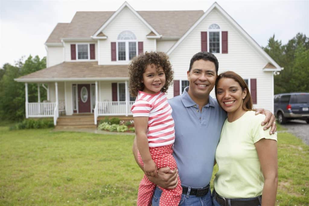 A smiling family standing in front of a two-story suburban home with a well-kept lawn