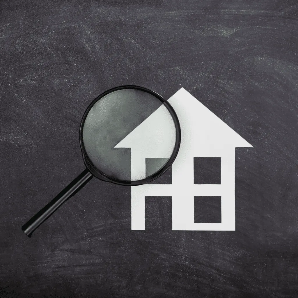 Magnifying glass over a simple house icon on a chalkboard background, symbolizing a roof inspectionv