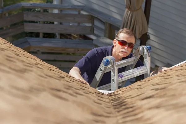 Home inspector on a ladder examining the condition of a roof for an Orlando roof certification inspection.