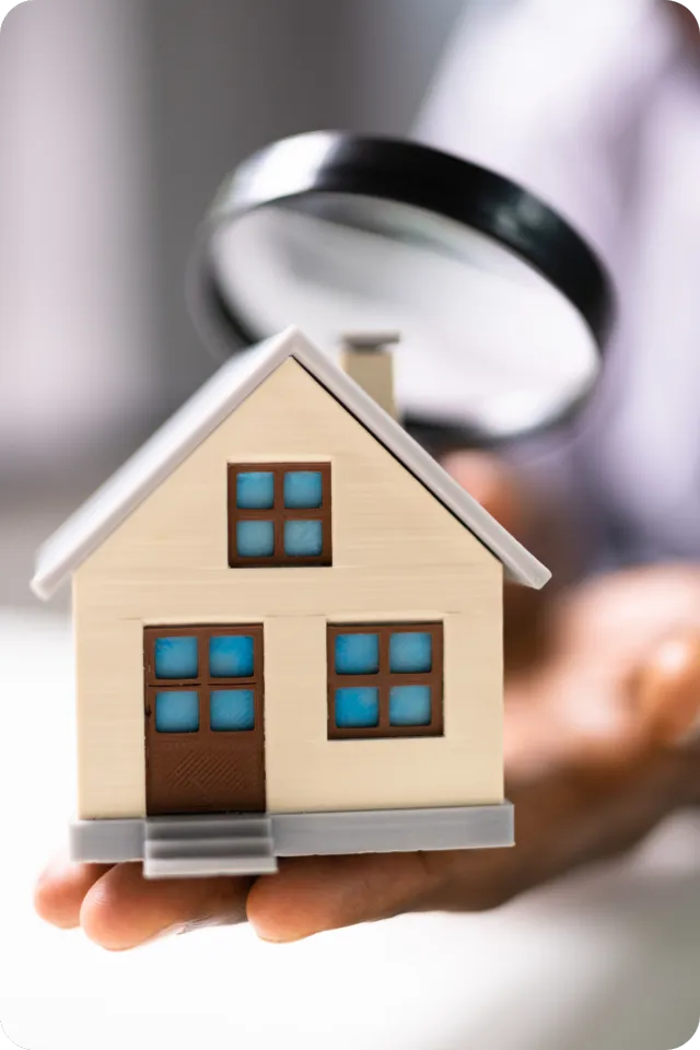 Person holding a small model house while inspecting it with a magnifying glass, symbolizing an 11-month builder warranty inspection in Winter Haven, FL.