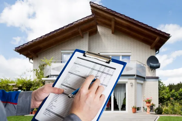 Home inspector holding a clipboard and taking notes in front of a suburban house during an Orlando 11th-month warranty inspection.