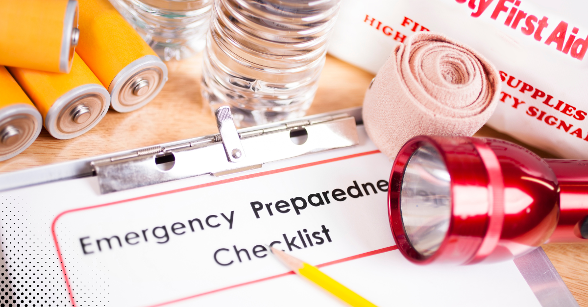 Emergency preparedness checklist surrounded by essentials like batteries, water, bandages, and a flashlight.